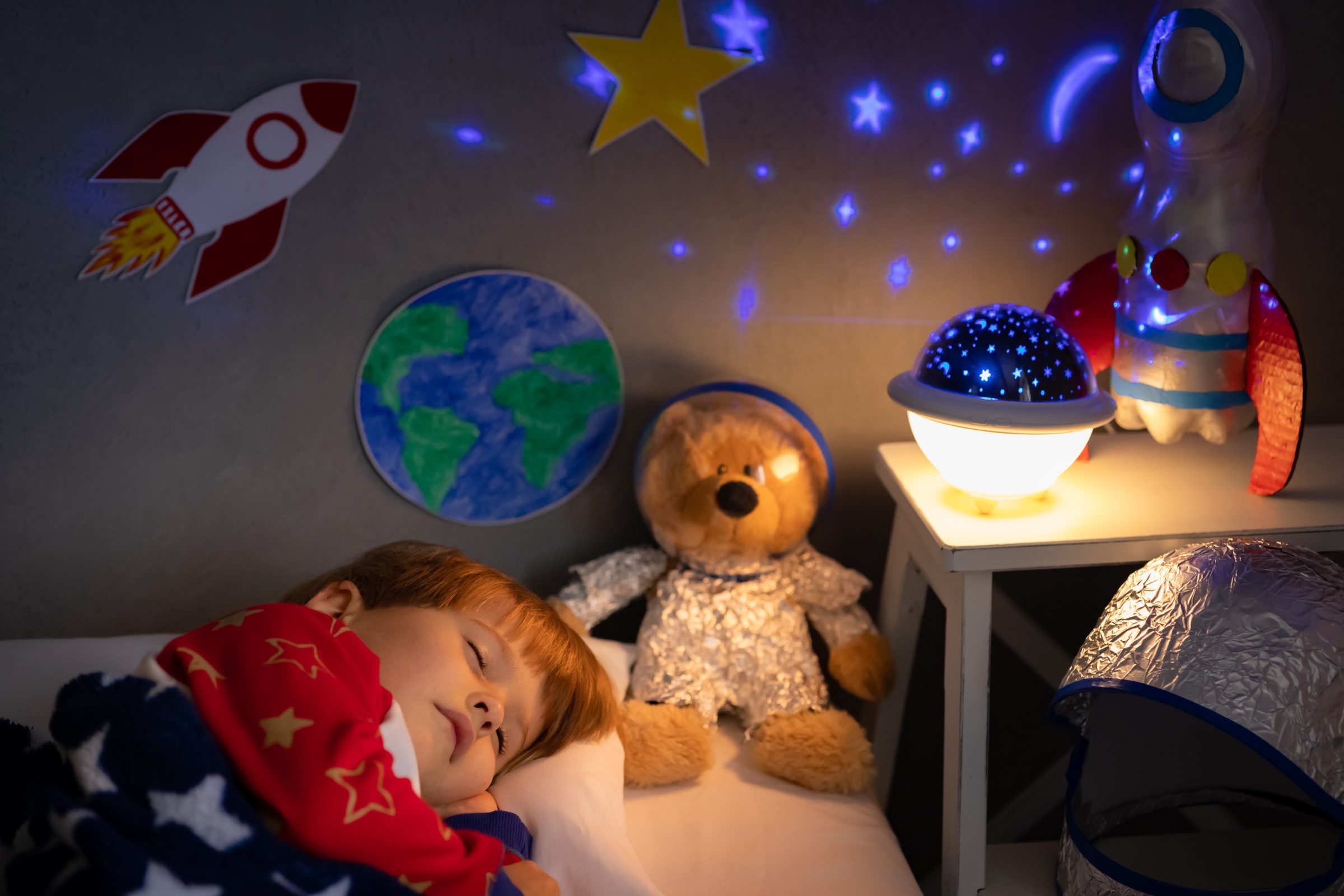 Child asleep in a space-themed bedroom beside a glowing night light