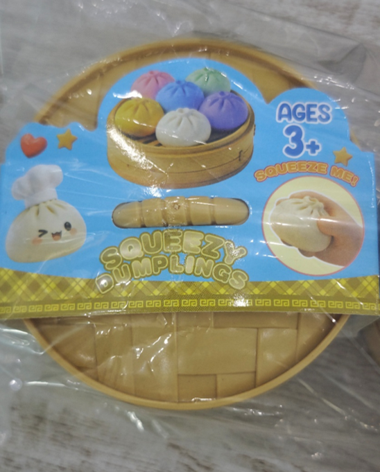 Retail packaging for Squeezy Dumplings, marked SQUEEZE ME and Ages 3+, showing multicoloured dumpling-shaped squishy toys in a bamboo steamer